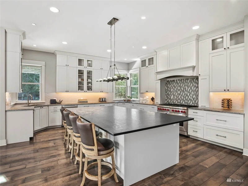 White kitchen with a broad dark island, pendant lights and wood floors