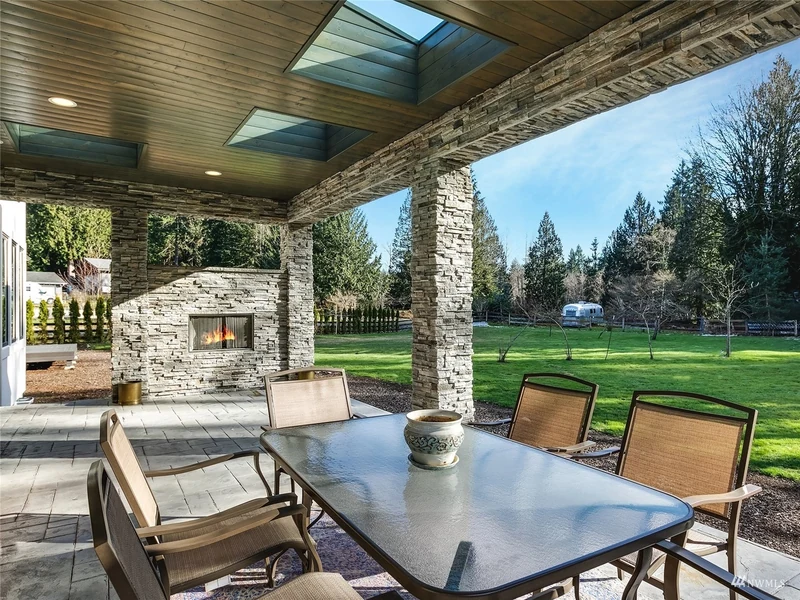 Covered outdoor dining patio with a stone fireplace overlooking the lawn