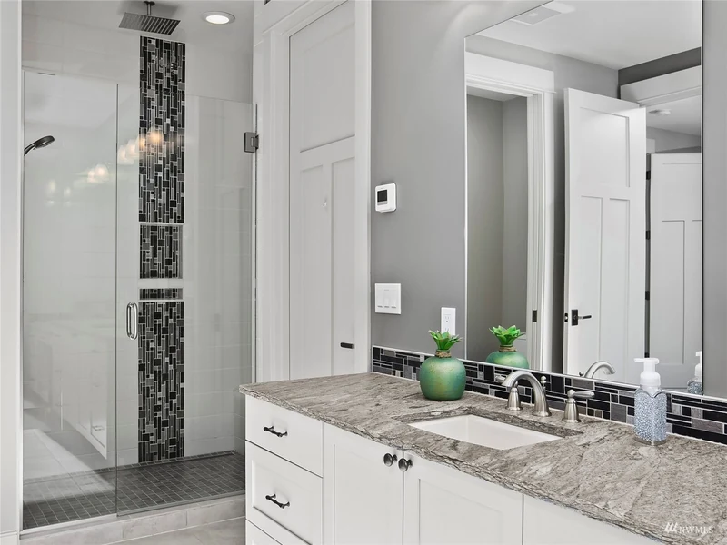 Bathroom double vanity beside a glass shower with decorative tile