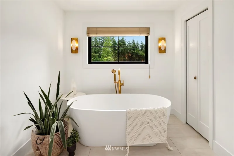 Freestanding bathtub beneath a window facing the trees