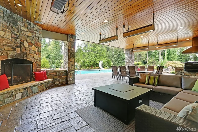 Covered outdoor lounge with a stone fireplace beside the pool